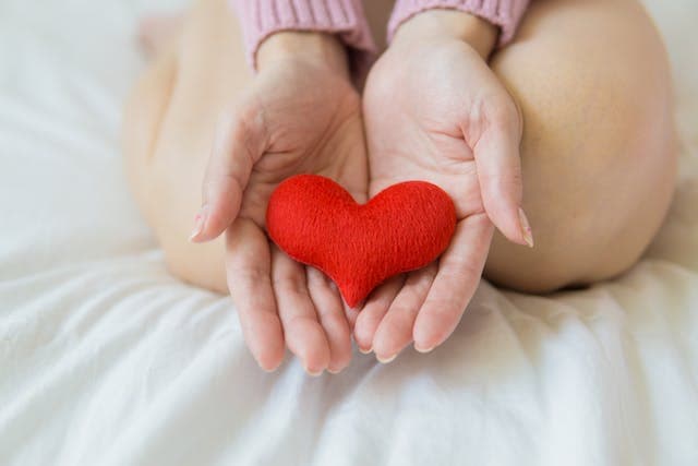 Woman holding a red stuffed heart in her two outstretched hands