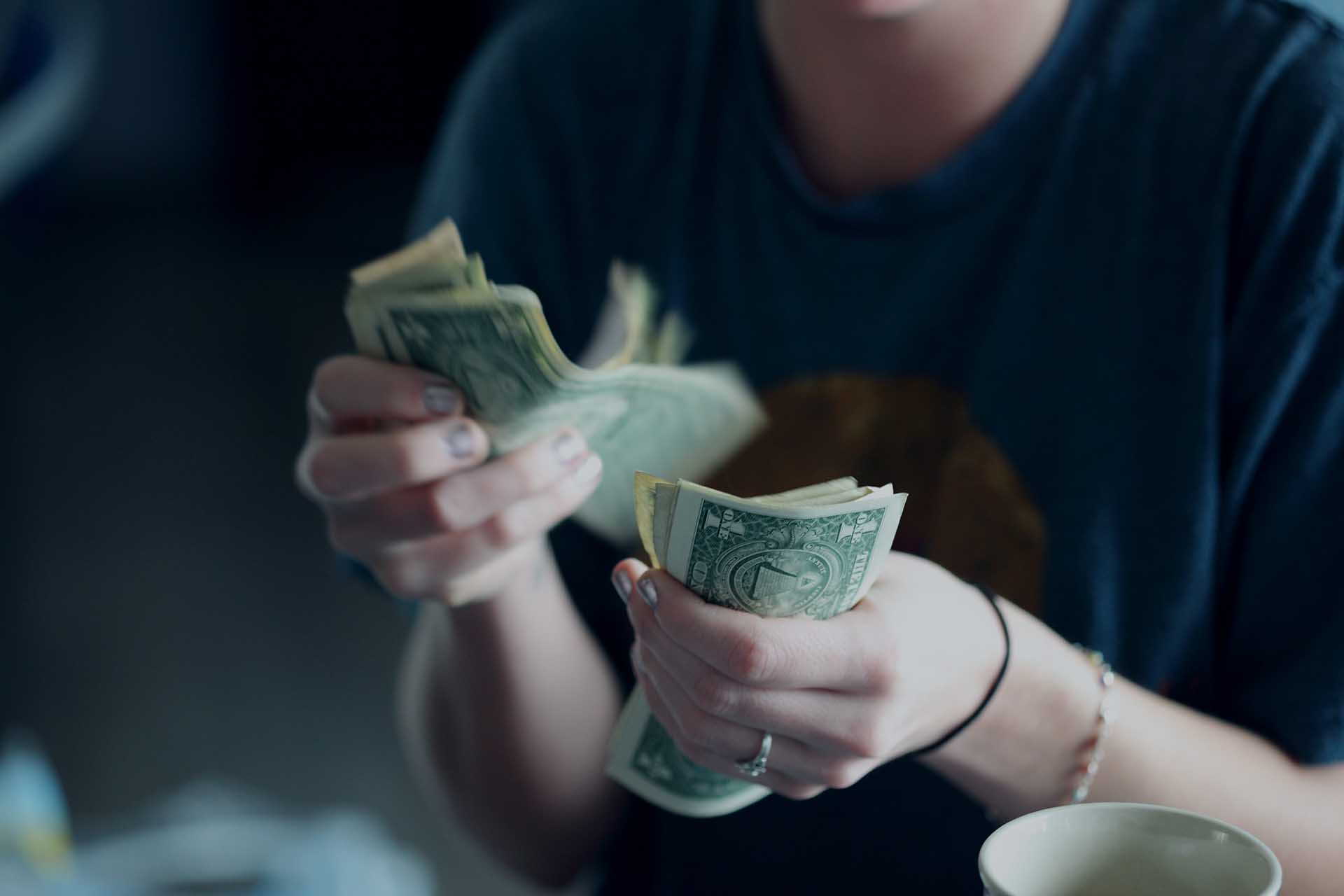 Woman in dark t-shirt counting dollar bills in her hand