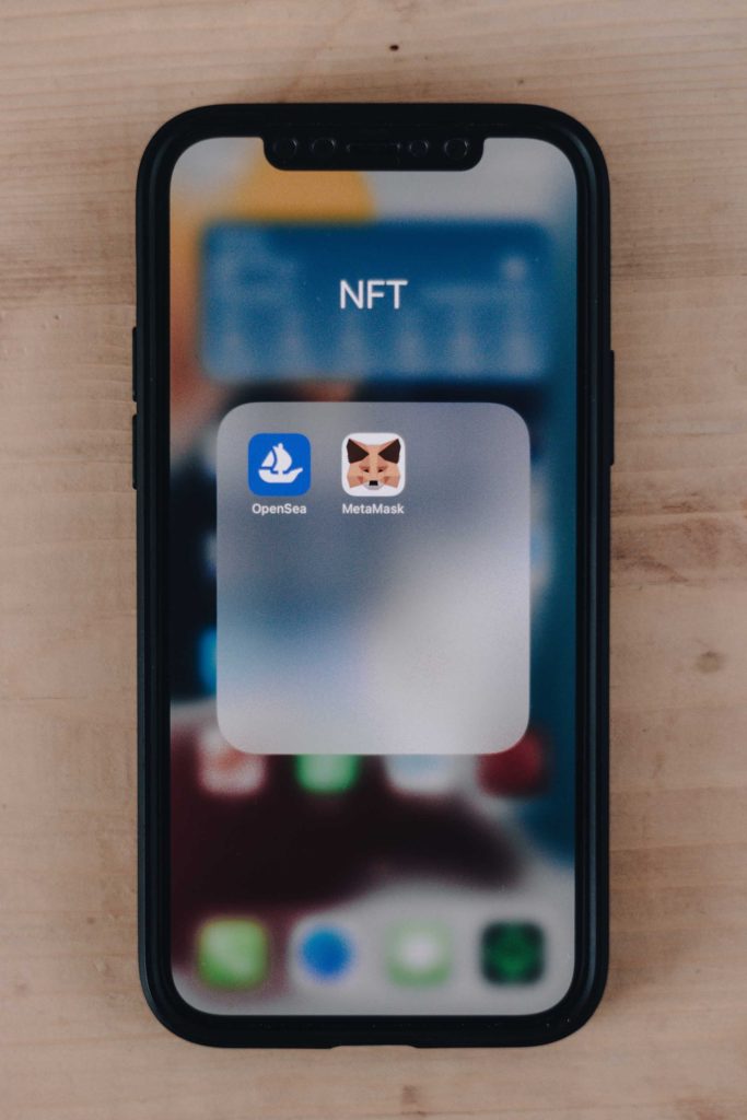 iPhone folder showing apps for OpenSea and MetaMask to buy digital real estate