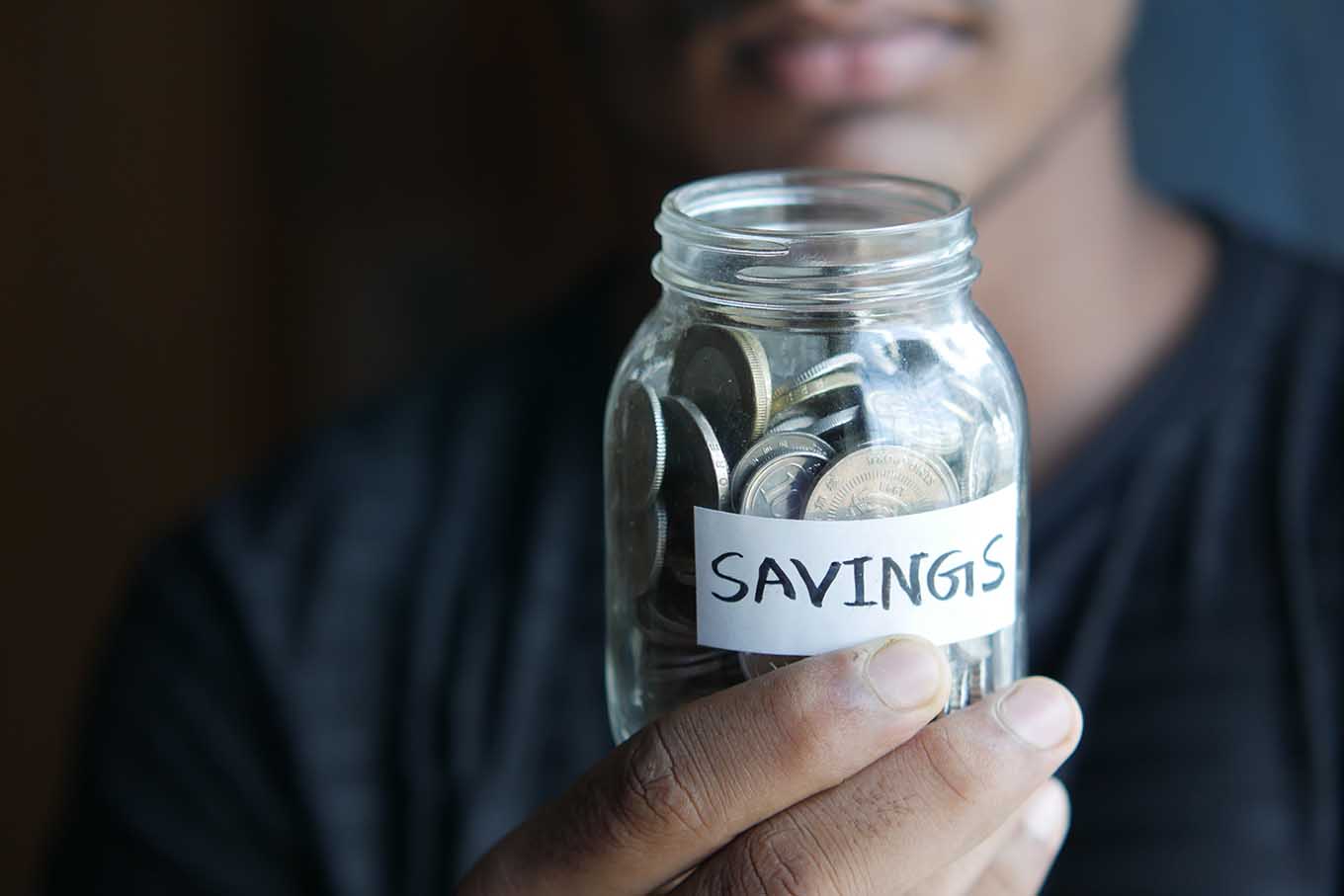 Man holding a jar full of change labeled savings