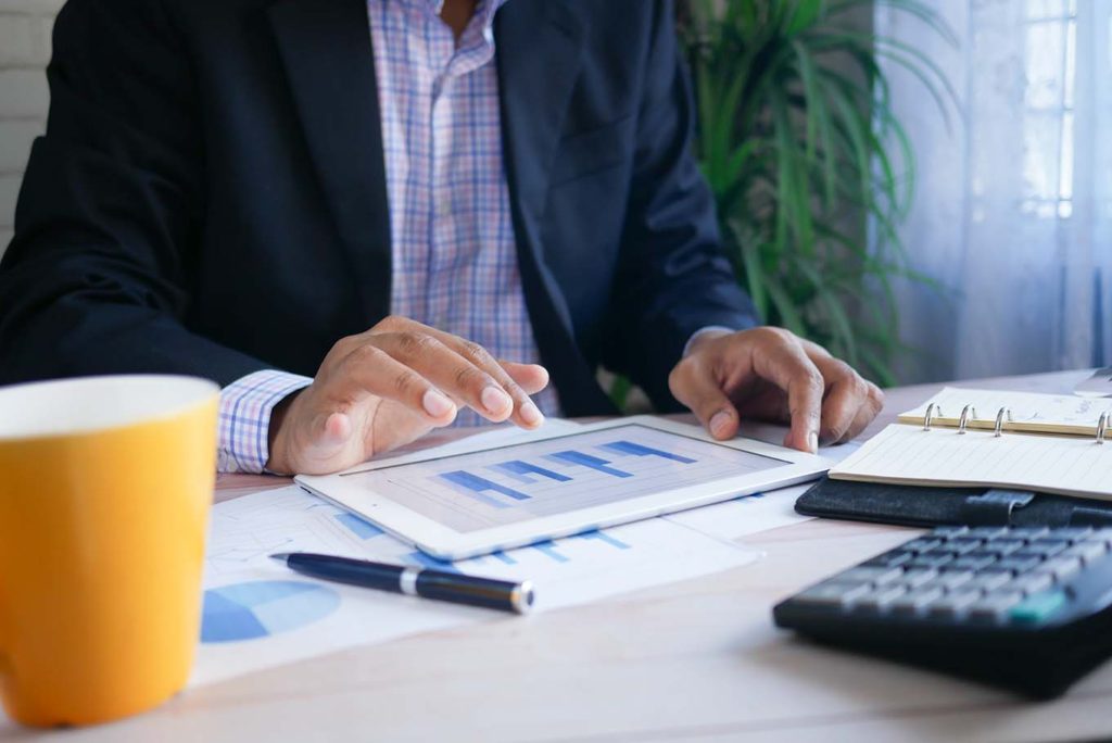 Data analyst reviewing graphs and taking notes on a white tablet